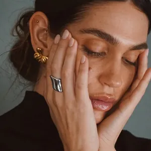Irregular glossy stainless steel ring and gold bow earrings on a model with soft lighting