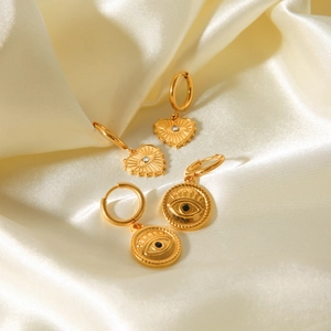 Macro view of gold heart and round devil eye earrings on white satin fabric
