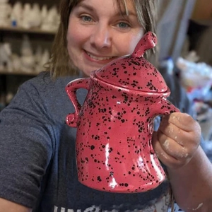 Pink ceramic canister with attitude and black spots held by hands in a studio