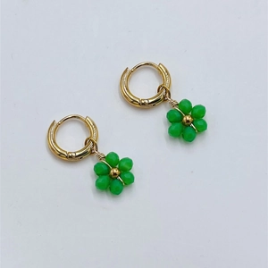 Detail view of gold hoop earrings with green beaded flower charms on white background