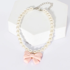 Detailed view of dog pearl necklace with pink bow pendant on white marble display