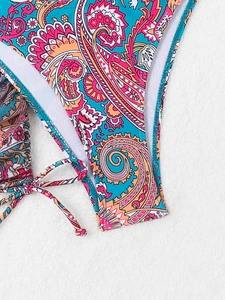 Close-up of paisley print bikini bottoms with adjustable side ties on white sand background