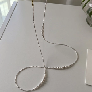 Detail of silver beaded pearl necklace featuring a golden clasp on a minimalist background