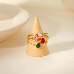 Close-up of four gold hammered rings with colorful pear-cut zircon stones on a wooden stand