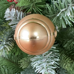 Close-up of golden festive football ornament hanging on a snowy Christmas tree branch