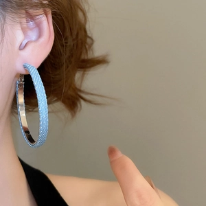 Nahaufnahme von blauen Creolen mit Denim-Textur, getragen von einem Modell für Chic