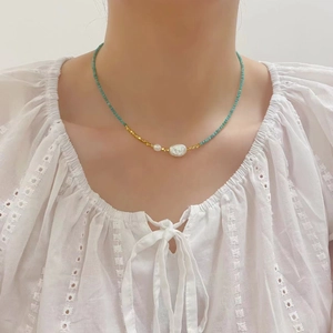 Close-up of tourmaline and freshwater pearls on a gold beaded necklace worn by a model