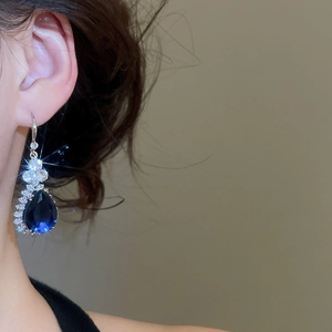 Detailed close-up of teardrop earrings with deep blue pear-cut stone and zircon cluster