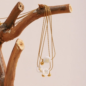 Detail of gold chain necklace with round white alphabet pendants on a dry branch