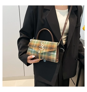 Detail of green plaid crossbody bag with gold letter logo and fringe tassel accessory