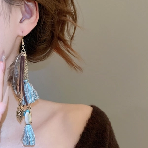 Detailed view of long bohemian tassel earrings with feathers and shells on a model