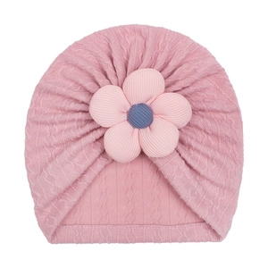Detailed view of pink knitted baby hat featuring a 3D floral accent and textured cable pattern
