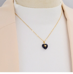 Detail of gold heart necklace with dark blue heart pendant worn on elegant model outfit
