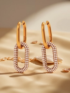 Détail macro de boucles d'oreilles créoles dorées ornées de zircons blancs sur sable beige