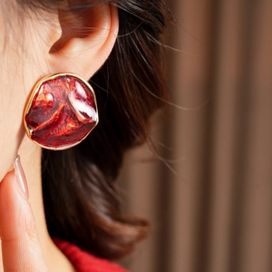 Close-up of red enamel irregular round stud earrings with gold metallic borders on model