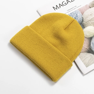 Detailed knit texture of bright yellow beanie hat with fashion magazine on white background