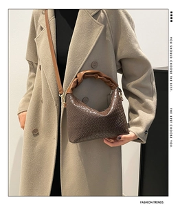 Detail of dark brown woven texture bucket bag with ruched handle on beige coat