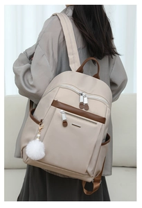 Beige commuter backpack for women with brown trim and white fuzzy pom pom keychain detail