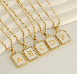 Detailed view of gold square shell pendants with letter engravings and crystal accents