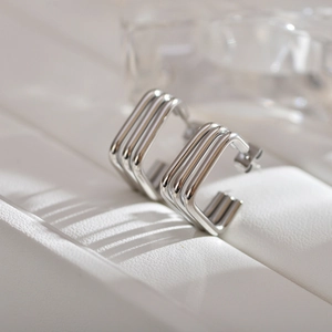 Detail of silver C-shaped geometric hoop earrings with textured parallel ribbing on a stand