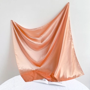 Detailed view of glossy salmon pink satin square scarf draped over a magazine