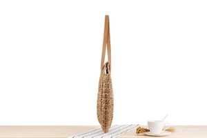 Detail of round straw shoulder bag with woven texture and brown leather strap on a table