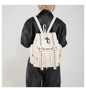Detail shot of a white punk backpack featuring silver studs and a black metal cross charm