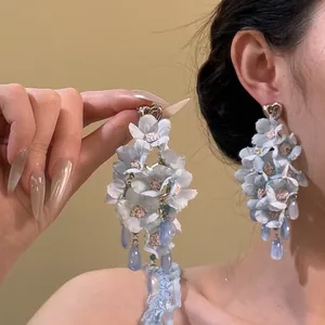 Détail de grandes boucles d'oreilles fleurs en tissu bleu avec pendentifs goutte d'eau
