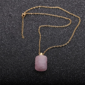 Flat lay macro of a pink crystal cylindrical perfume bottle pendant with golden chain
