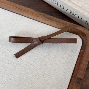 Close-up of a vintage brown leather bow hair clip on a wooden linen display tray