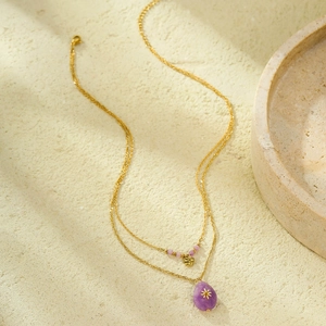 Double-layered gold necklace with purple teardrop gemstone and heart pendant on stone