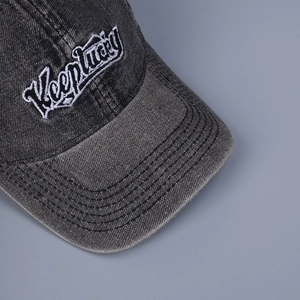 Detail of Keeplucky 3D white embroidery on a distressed dark gray denim baseball cap
