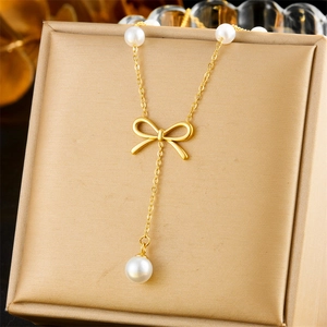 Collier doré avec nœud et pendentif perle blanche présenté sur un coffret cadeau doré