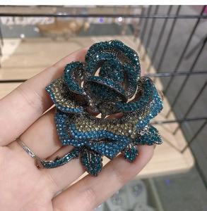 Detailed view of handcrafted rose brooch with blue and champagne rhinestones held in hand