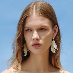 Elegant white petal drop earrings with gold metal and pearls worn against a blue sky background