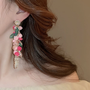 Detail of floral earrings featuring resin roses and crystal tassels on a female model