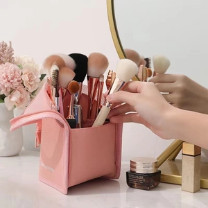 Pink mesh makeup brush holder standing on a vanity desk with various brushes inside