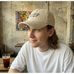 Close-up of beige distressed baseball cap with blue GUZF embroidery and worn-out details