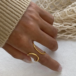 Minimalist double-layered gold open ring shown on a finger with warm textured background