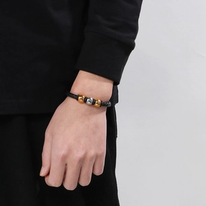 Detail of men's braided black leather bracelet with gold and silver metal beads