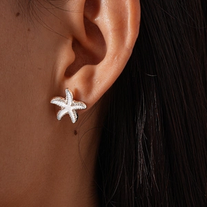 Close-up of a stylish gold starfish stud earring with faux pearl on model's ear