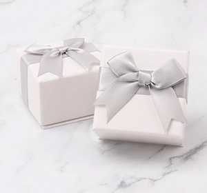 Close-up of white jewelry gift boxes with silver-gray ribbon bows on marble background