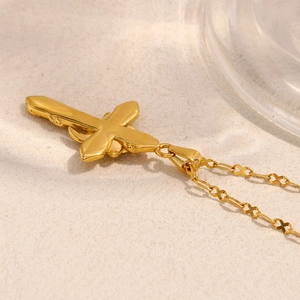 Detailed close-up of a 18K gold plated stainless steel cross pendant necklace on a beige base