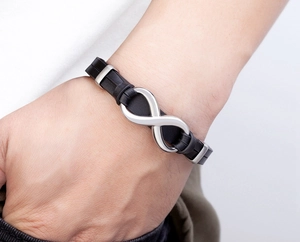 Detail of mens black braided leather bracelet featuring a stainless steel infinity symbol