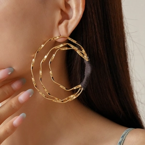Close-up of model wearing large gold multi-layered twisted hoop earrings with thread detail