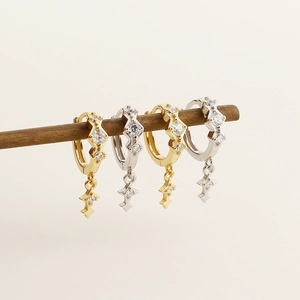 Dettaglio di orecchini pendenti a croce e stella in argento e oro con pavé di cristalli