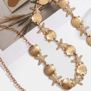 Detail of gold waist chain with seashell, starfish charms and pearls on a white background