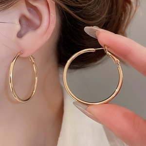Close-up of oversized gold geometric hoop earrings on a model showing polished finish