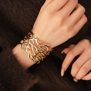 Golden wide open bangle with coral hollow design on luxury warm fabric background