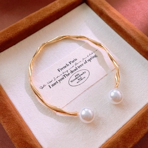 Close-up of golden wavy cuff bracelet with white pearls in a premium jewelry box display